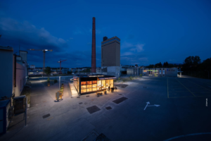 Site bluefactory Fribourg au levé du jour, bâtiment central éclairé avec cheminée classée au patrimoine en arrière plan
